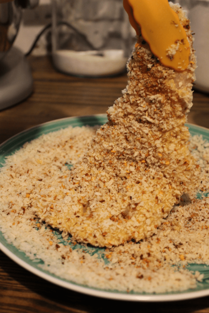 tongs holding breaded chicken