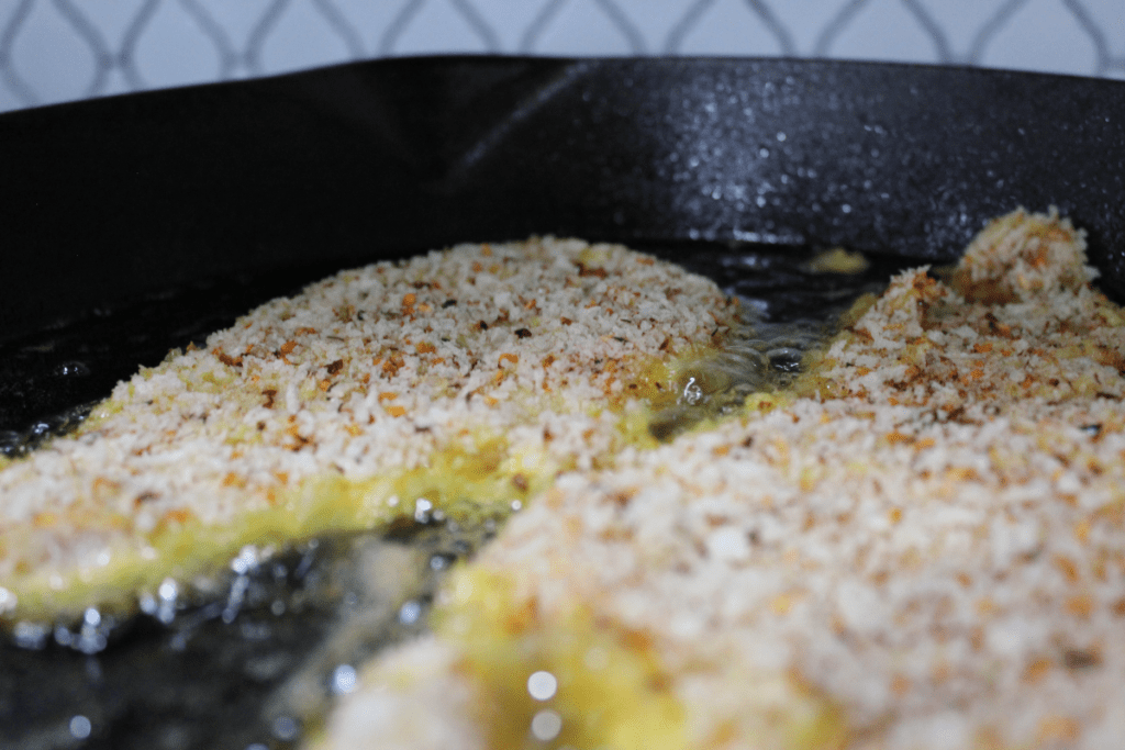 breaded chicken just placed in oil in cast iron skillet, close up