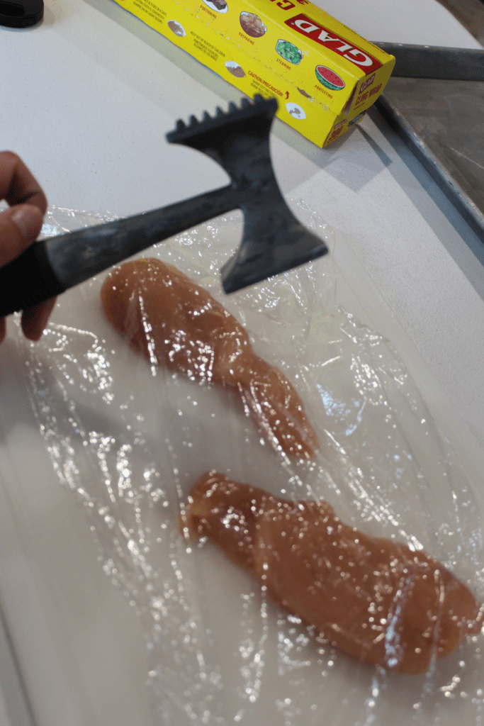 chicken breast with plastic wrap cover, kitchen mallet shown