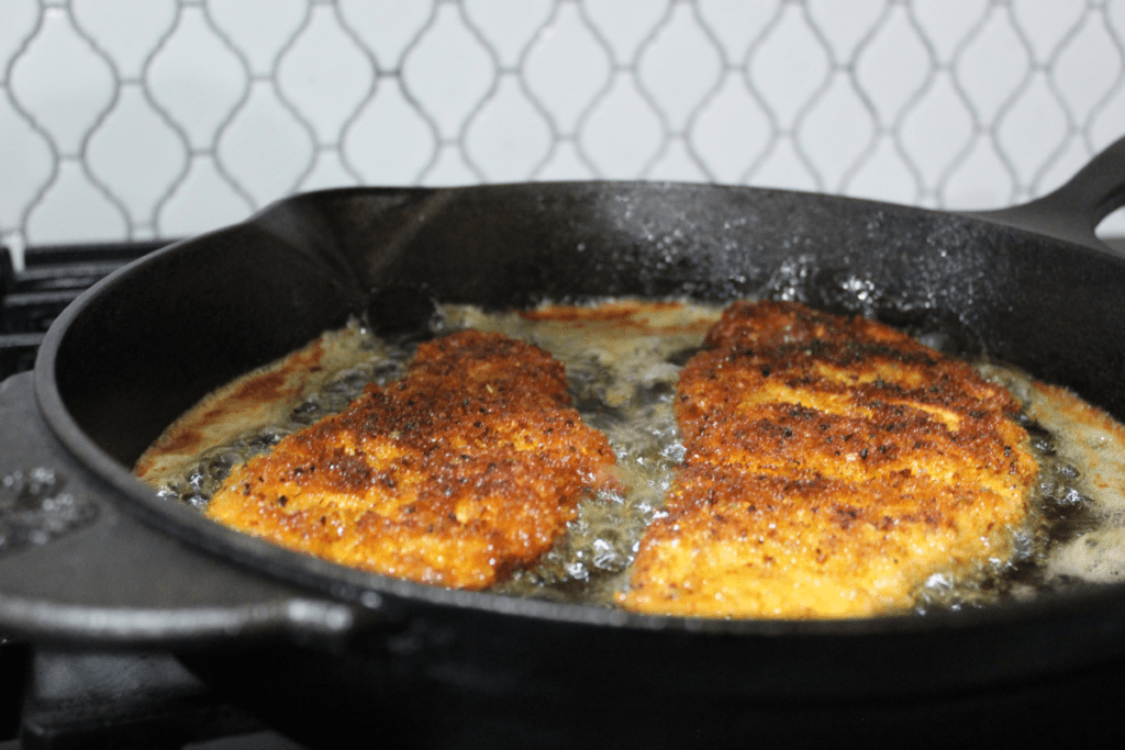 Golden brown chicken in oil in a cast iron skillet