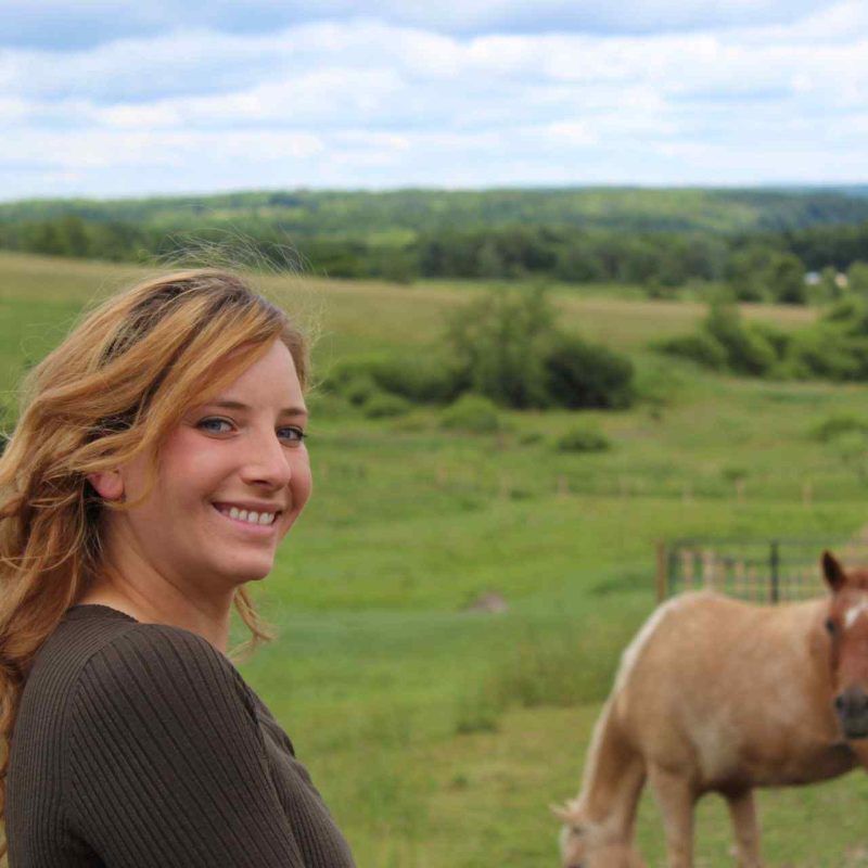 Kristy standing in a filed with two horses.